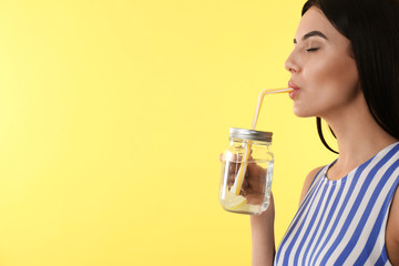 Beautiful young woman drinking tasty lemon water on yellow background, closeup. Space for text