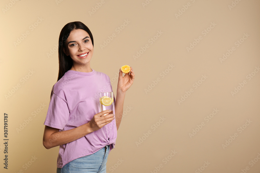 Wall mural Beautiful young woman with tasty lemon water and fresh fruit on beige background. Space for text