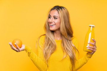 Young blonde woman holding an orange juice over yellow background