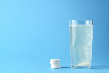 Glass of water with an effervescent tablet on a blue background