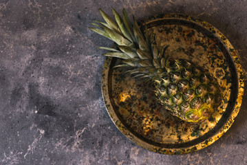  Fresh tropical fruit pineapple on a round plate on a gray background. Place for your text.