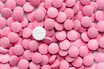 Pile of pink pills and around a white one. Medication, self-treatment or placebo concept: one tablet is different from the lot of others - obrazy, fototapety, plakaty
