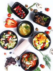 Culinary dishes made from natural products in a plastic bowl on the background with ingredients for cooking. Healthy food delivery concept. Top view.