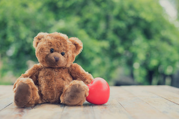 Brown cute teddy bear with red heart on on nature background with sweet and romantic moment.