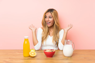 Young blonde woman having breakfast milk with surprise facial expression