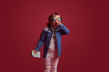 A little fashion girl holding dollars on pink background