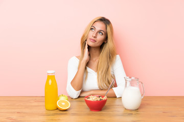 Young blonde woman having breakfast milk thinking an idea