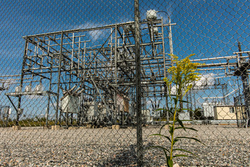 low angle view through the exterior metal fence of an electrical substation, generation, transmission, and distribution system Elements