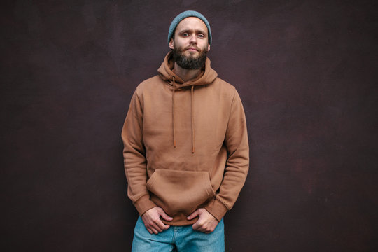 City portrait of handsome hipster man with beard wearing brown blank hoodie or hoody with space for your logo or design. Mockup for print