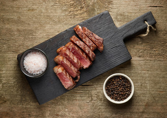 Sliced grilled beef steak with salt and pepper on wooden background