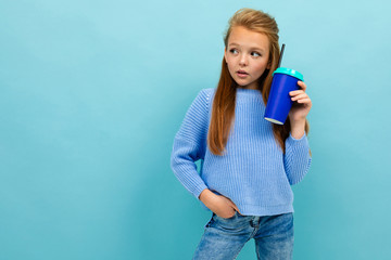 portrait of a stylish european girl drinking holding a glass on a light blue wall with copyspace