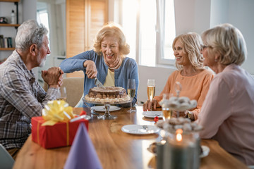 Happy senior woman cutting cake while celebrating birthday with friends at home.