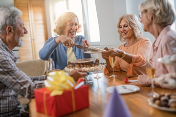 Happy mature woman serving birthday cake to her friends at home.