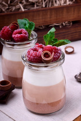 Three chocolate mousse dessert in a glass jar topped with frozen raspberries and mint