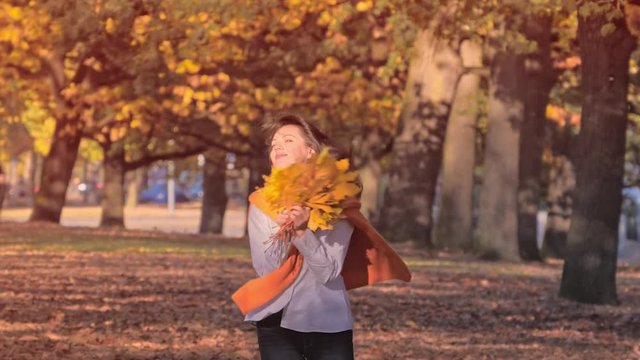 Young woman walking in park with a bouquet of yellow autumn leaves