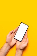 Male hands hold a modern black smartphone with white blank screen on yellow background. Modern technology, phone, gadget in hands, touch screen, template for your design. Mockup