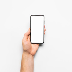 Male hands hold a modern black smartphone with white blank screen on light gray background. Modern technology, phone, gadget in hands, touch screen, template for your design. Mockup