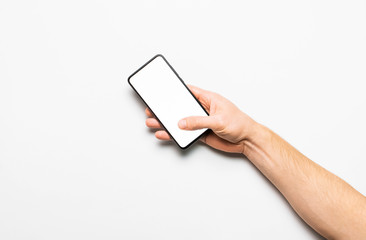 Male hands hold a modern black smartphone with white blank screen on light gray background. Modern technology, phone, gadget in hands, touch screen, template for your design. Mockup