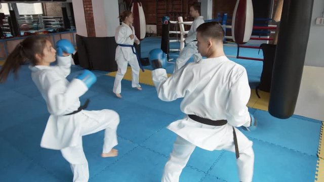 Wide shot of two pairs of sparring partners wearing white kimonos exercising in gym