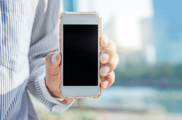 close up business man using hand hold smartphones with blank screen outdoor in city with sunrise and building background. 5G technology connecting the world.