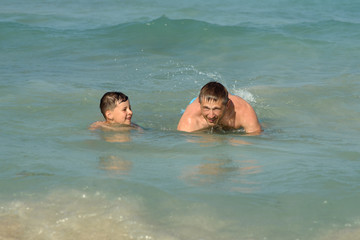 European man is happy to spend his summer holidays with his son. They are swimming in the ocean and enjoying pastime.