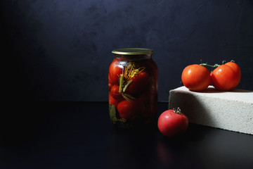 Preserved and fermented organic tomatoes in glass jar on dark background. Canned food concept. Conservation of farm harvest. Conserved vegetables 