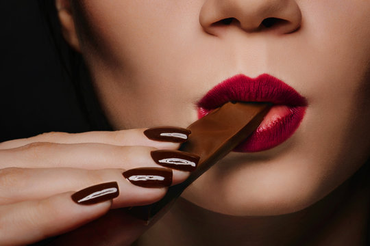 Beautiful sexy woman with brown manicure eat dark chocolate, red lips with red lipstick
