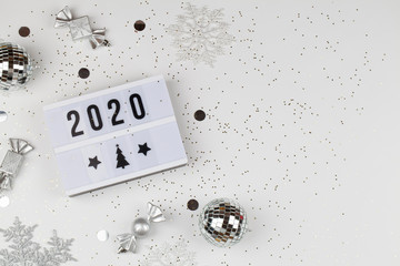 figures 2020 on light box with white snowflakes, balls, and decorations on white background with gold stars