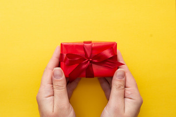 Top view of female hands holding gift red box with ribbon bow isolated over blue background, copy space.