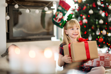 Young happy girl sitting with christmas present looking away