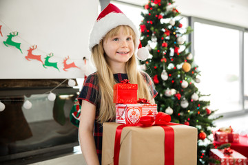 Young happy girl in santa hat holding lot of christmas gifts