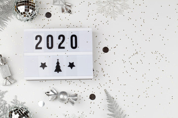 figures 2020 on light box with white snowflakes, silver tree branches and decorations on white background