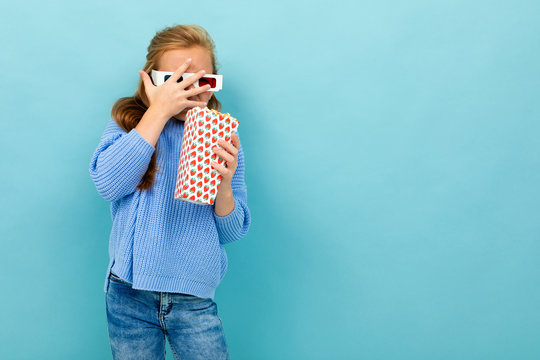 Attractive Girl In Movie Glasses Is Holding Popcorn In Her Hands On A Light Blue Studio Background