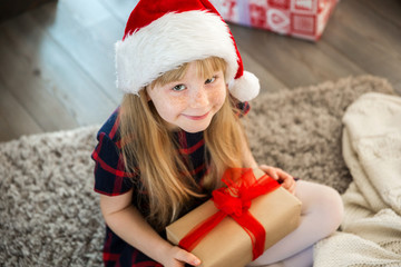 Girl in santa hat holding present sitting on floor