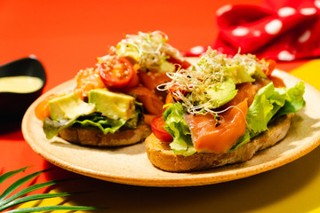 Two open face gravlax salmon sandwiched on red yellow background