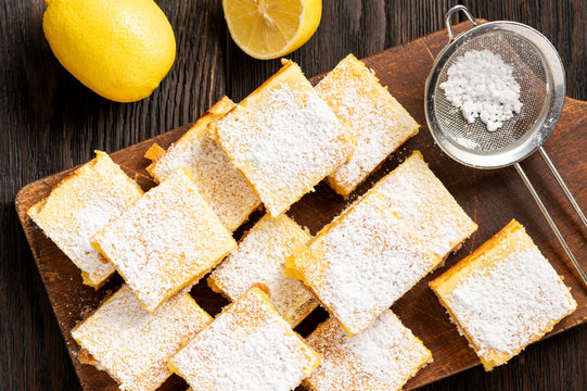 Homemade lemon bars with shortbread crust, on wooden background. 