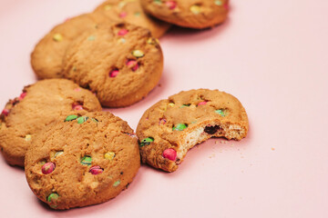 Oatmeal cookies with colorful drops on a pink background. Bitten biscuits.