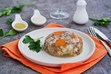 Cold appetizer, portioned meat jelly of pork, beef and chicken on a white clay plate on a gray concrete background. Holiday appetizer for New Year. Russian cuisine. Selective focus.