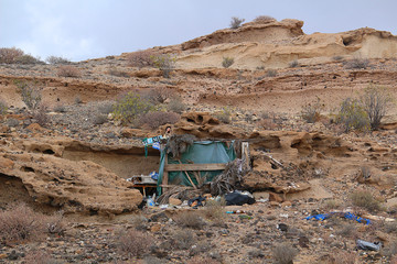 Meager self-made dwelling of dropouts in a rock face with rubbish dumped around