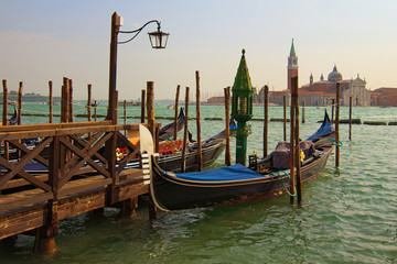 Fototapeta na wymiar Beautiful landscape view of Venetian Lagoon. Moored gondolas near wooden pier. San Giorgio Maggiore church at the background. Venice, Italy. Famous touristic place and travel destination in Europe