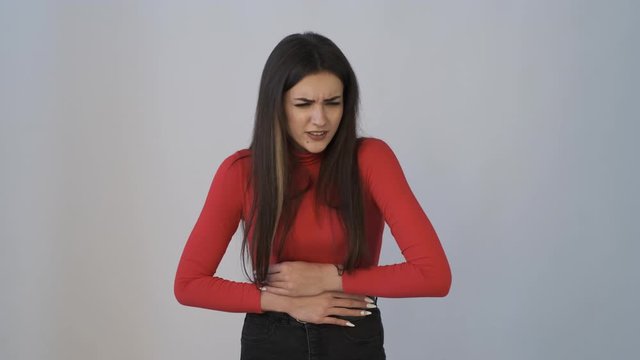 Brunette girl is frowning and suddenly feeling acute pain in her stomach, holds hands for her belly
