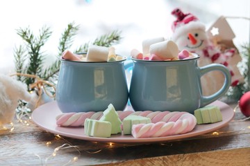 Two cups with a drink and marshmallows, Christmas decor, illuminations on a wooden windowsill, the concept of home comfort, winter holidays