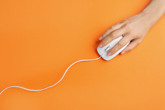 Woman using modern wired optical mouse on orange background, top view
