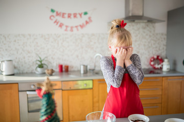 Young girl in red apron standing in kitchen covering her face