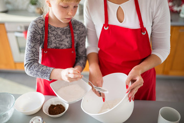 Young girl helping mom pouring sugar to bowl with flour