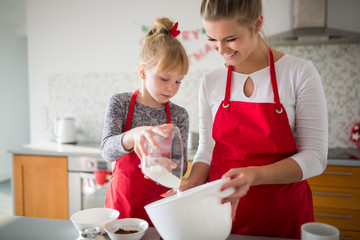 Young girl pouring flour to her mom bowl