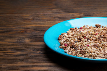 Muesli flakes in blue plate on wooden background closeup