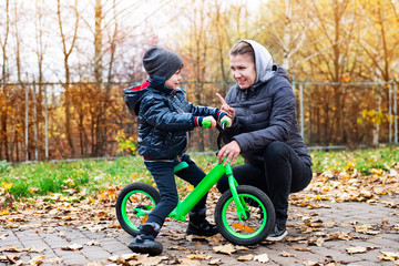 A woman and a little boy walk together in an autumn city, a boy rides a bicycle and his mother tells him to be careful