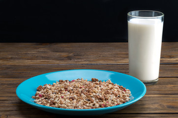 Muesli flakes in blue plate and glass of milk on wooden background closeup