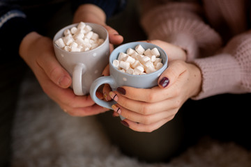 Happy couple's hands holding hot cups with hot drinks with marshmallow.